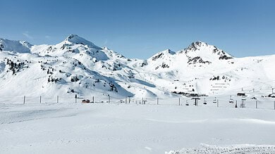 Snow-covered mountain landscape with ski slopes and chairlifts under a clear blue sky, ideal for winter sports and skiing activities.