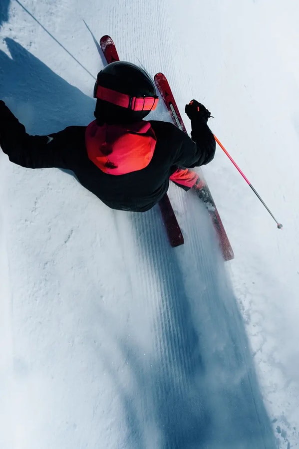 Skiing enthusiast carving fresh powder on a pristine winter slope, dressed in vibrant winter gear, showcasing the thrill of winter sports and the beauty of snowy landscapes.