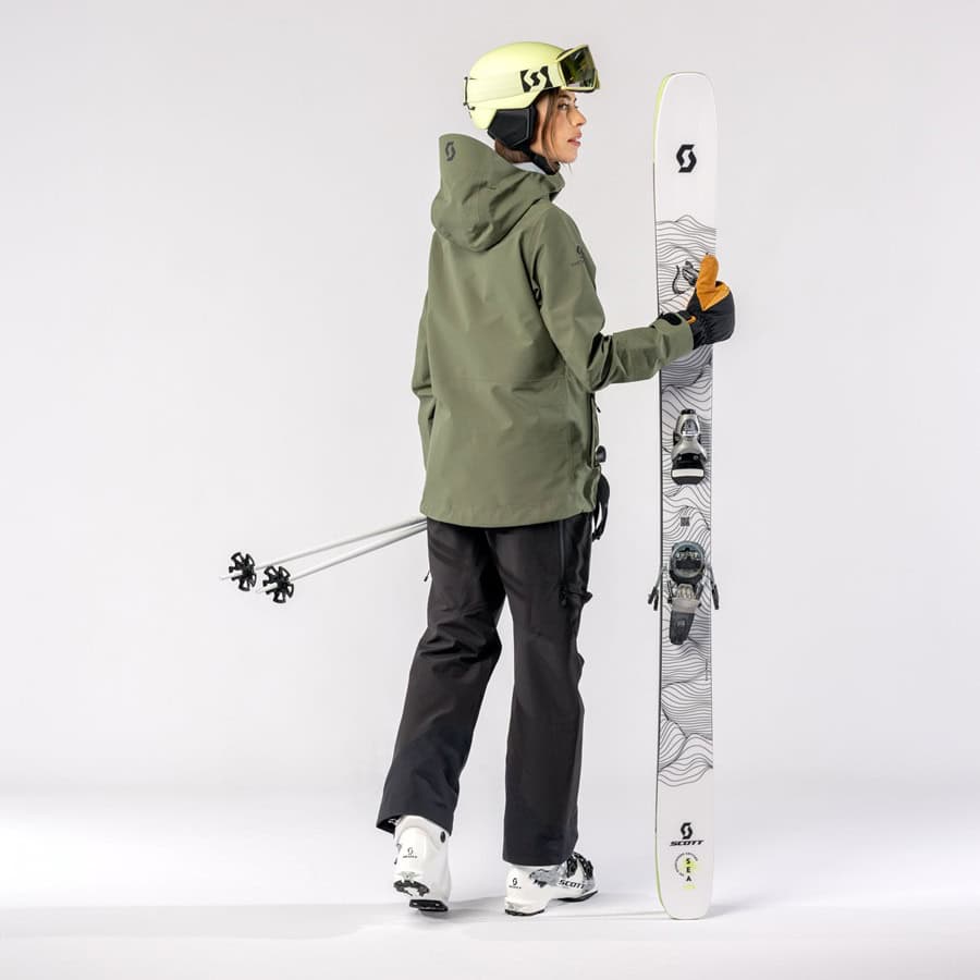 High-quality female skier holding a snowboard, dressed in winter sports gear including helmet and goggles, ready for winter adventure on snow-covered slopes.