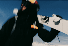 Ski enthusiast holding a snowboard in winter sports gear against a snowy mountain backdrop, representing everything winter for winter sports lovers.