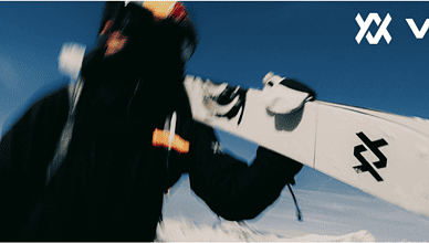 Ski enthusiast holding a snowboard in winter sports gear against a snowy mountain backdrop, representing everything winter for winter sports lovers.