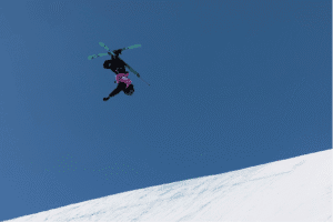 Jumping skier performing a mid-air trick against a clear blue sky, showcasing winter sports excitement.