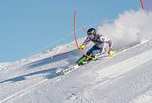 Skier navigating through a slalom gate on a snowy mountain slope during a competitive alpine skiing event, showcasing precision and speed in winter sports.
