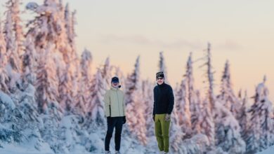 Snowy forest landscape with two hikers in winter outdoor gear enjoying the scenery during sunset. Winter in the mountains, with snow-covered trees and a beautiful sky.