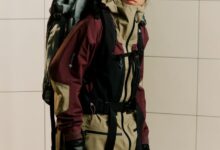 Backpacker in winter sports gear, wearing goggles and gloves, standing indoors, ready for winter adventure, showcasing premium winter clothing and equipment for snow and cold weather conditions.