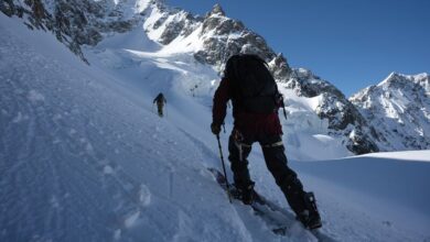 Deep snow mountain climbing in winter, two climbers ascending snowy slopes under clear blue sky, showing adventure, winter sports, and mountain exploration.