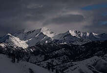 Bright snow-covered mountain peaks under a moody cloudy sky, showcasing winter mountain scenery and outdoor winter landscapes.