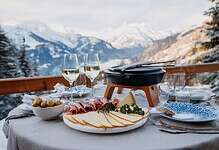 Elegant winter mountain outdoor dining setup with cheese, cold cuts, and wine in snowy Alps, perfect for winter holiday meals.