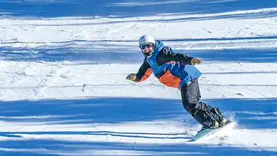 Vibrant skier in colourful winter gear gliding down snow-covered slopes on a sunny day, showcasing perfect winter sport conditions.
