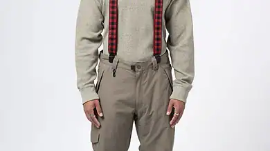 Stylish young man wearing beige cargo pants, grey sweater, and red checkered suspenders, showcasing winter fashion and outdoor wear essentials.
