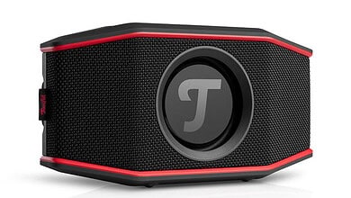 Portable black and red speaker with a circular logo in the centre, designed for outdoor winter activities and music enjoyment, perfect for winter sports and celebrations.