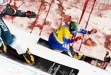 Fast alpine skier in action during a race, demonstrating skills and speed on snow, with a bright blue safety fence in the background, capturing the excitement of winter sports.