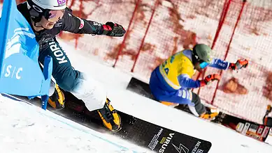 Fast alpine skier in action during a race, demonstrating skills and speed on snow, with a bright blue safety fence in the background, capturing the excitement of winter sports.