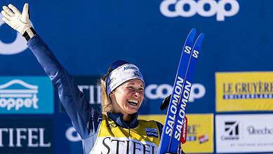 Excited female skier celebrating victory on podium at winter sports event with blue background and sponsor banners.