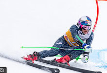 Red Bull alpine skier racing downhill on snowy slope during alpine skiing competition.
