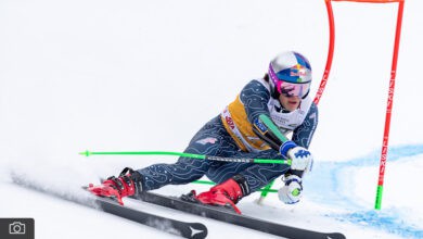 Red Bull alpine skier racing downhill on snowy slope during alpine skiing competition.