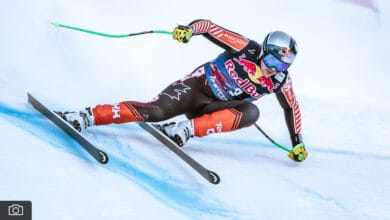 High-speed alpine skier in Red Bull gear making a sharp turn on snowy slope during winter sports competition.