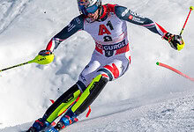 A skier racing down a snowy mountain slope, wearing a USA team outfit with red, white, and blue, using leki poles, showcasing winter sports and skiing expertise.