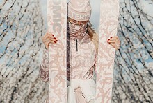 1. Person holding pink skis outdoors during spring with blossoming trees and blue sky, promoting winter sports gear and accessories for winter adventures.