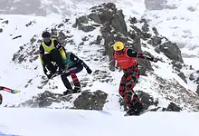 Skier jumping off a snow ramp during a freestyle skiing competition in snowy mountain terrain, showcasing winter sports excellence.