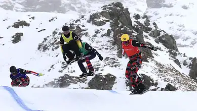 Skier jumping off a snow ramp during a freestyle skiing competition in snowy mountain terrain, showcasing winter sports excellence.