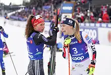 1. Female biathlon athletes exchanging high-fives after a race on snowy winter terrain at a competitive winter sports event. 2. Celebrating female biathlon athletes on a winter racecourse, highlighting victory and sportsmanship at a premier winter sports event. 3. Two female biathlon competitors sharing a joyful moment during a winter sports race with snow-covered grounds, race bibs, and supportive spectators in the background.