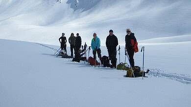 A group of hikers with trekking poles in a snowy mountain landscape under a clear blue sky, exploring winter adventures on snow-covered peaks.