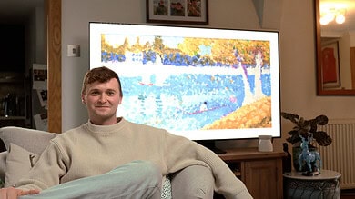 Young man sitting comfortably on sofa in living room, watching television displaying a colourful winter landscape scene.