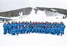 The Stifel U.S. Ski Team alpine athletes in blue gear pose together on snowy slopes with ski lifts and forested mountains in the background.