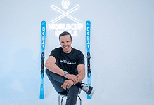 A comfortable man sitting with skis and poles in a winter studio, promoting winter sports gear and accessories for winter enthusiasts.