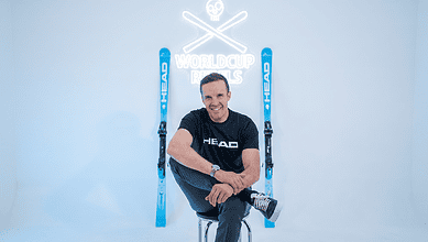 A comfortable man sitting with skis and poles in a winter studio, promoting winter sports gear and accessories for winter enthusiasts.