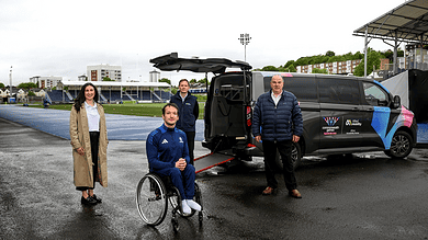 Accessible sports team with a wheelchair athlete and support staff at an outdoor stadium, showcasing winter sports equipment and inclusive athletic opportunities.