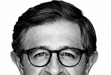 Black and white portrait of a middle-aged man with glasses, smiling gently, wearing a collared shirt.