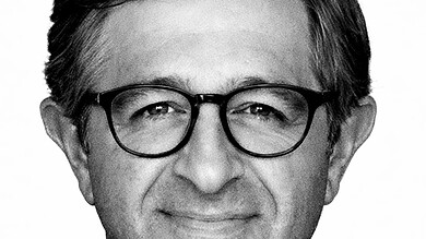 Black and white portrait of a middle-aged man with glasses, smiling gently, wearing a collared shirt.