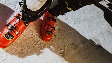 Close-up of a skier's foot wearing a Nikolai Schirmer Zero Cushion Pro Series Snow Sock and ski boot on snow.