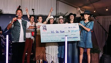 Group of women and men celebrating on stage with a large check for US Ski Team at a winter event.