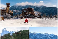 Snowy ski resort with mountains, skiers, and a helicopter flying over a forested area.