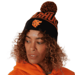 Woman wearing a black and orange knit beanie with a pom-pom and a bear mascot logo, paired with an orange hoodie.