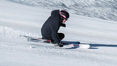 Skier in black winter gear carving through fresh snow on a clear day in the mountains.