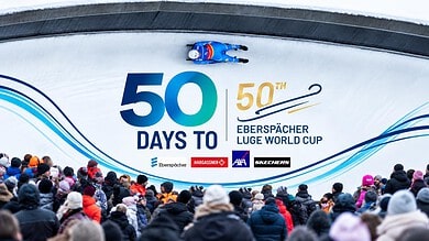 Crowd watching a luge race at the Eberspächer Luge World Cup with a large banner displaying '50 Days To' and event logos.