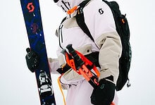 Snowboarder in winter gear holding a snowboard and ski poles, ready for winter sports on a snowy mountain.