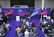 Audience watching a panel discussion at the mountain theatre during a winter sports event, with screens displaying promotional content and a scenic mountain backdrop.
