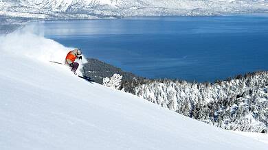 Skier descending a snowy mountain slope with a stunning lake and snow-covered mountains in the background, capturing the thrill of winter sports.