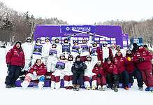 Group of winter sports athletes and coaches celebrating on snow with medals and trophies at Waterville Valley Resort.