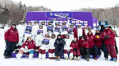 Group of winter sports athletes and coaches celebrating on snow with medals and trophies at Waterville Valley Resort.
