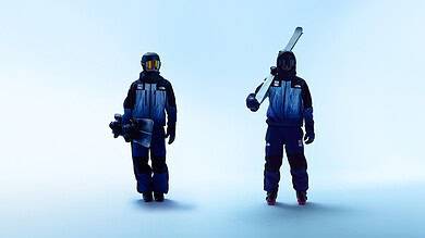 Two snowboarders in blue winter outfits standing on a pale blue background, one holding a snowboard and the other with a ski pole.