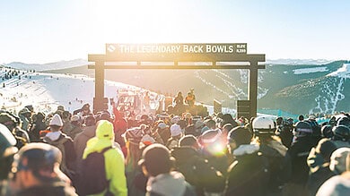 Crowd of skiers and snowboarders at the legendary Back Bowls ski event with scenic mountain views in the background.